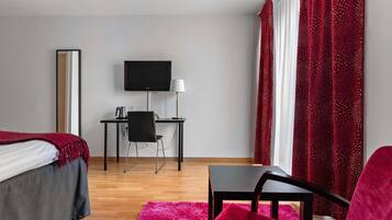 Una camera d'albergo con un letto, una scrivania, una sedia, televisore e tende rosse.