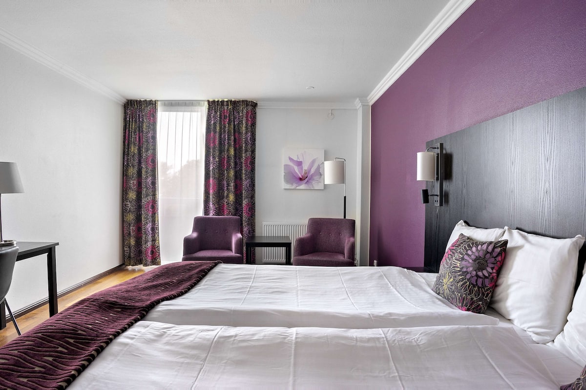 A hotel room with a large bed, two armchairs, a small table, and a lamp.