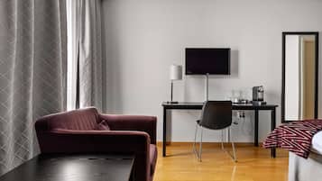 Ett hotellrum med ett mörkt skrivbord i trä, en svart stol, en tv som är monterad på väggen och en säng med ett mönstrat överkast.