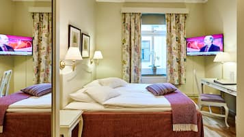 Ein Hotelzimmer mit zwei Betten, einem Schreibtisch, einem Stuhl, einem Fernseher und einem Fenster mit Vorhängen.