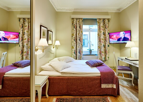 Habitación de hotel con dos camas, un escritorio, una silla, televisión y ventana con cortinas.