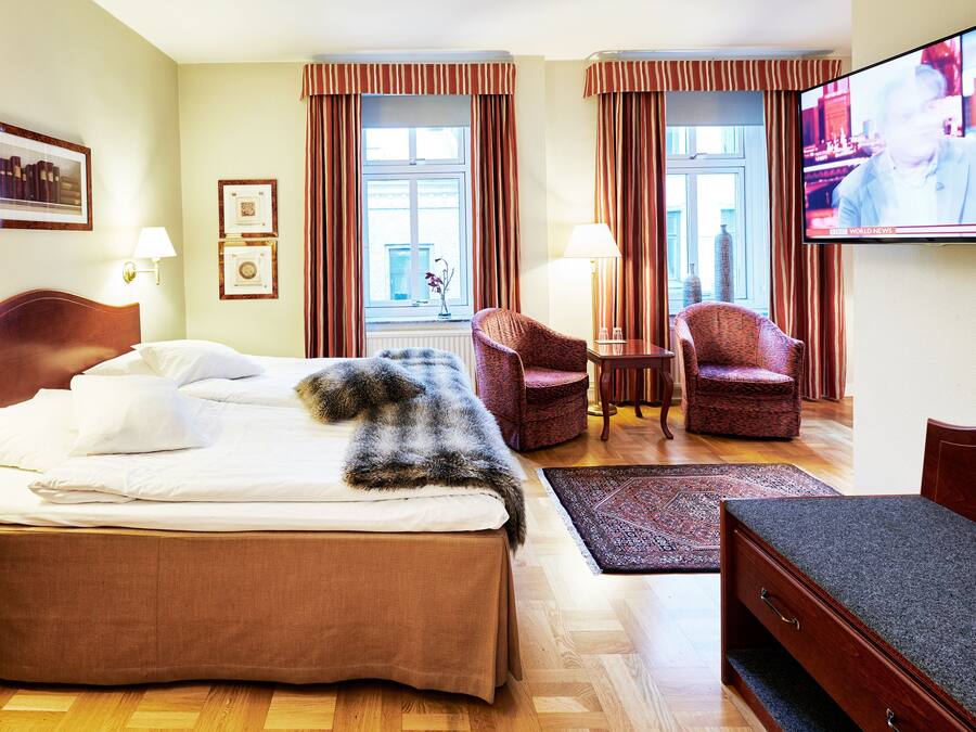 Habitación de hotel con una cama, dos sillones, una mesita, un televisor y una ventana con cortinas.