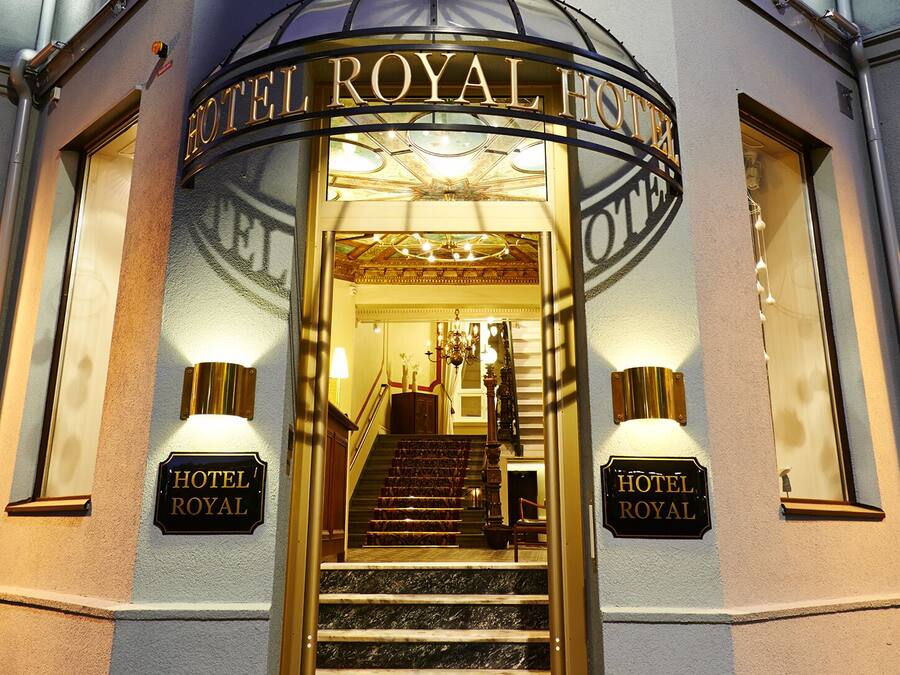 The entrance to Hotel Royal with a grand staircase, illuminated signs, and a classic architectural design.