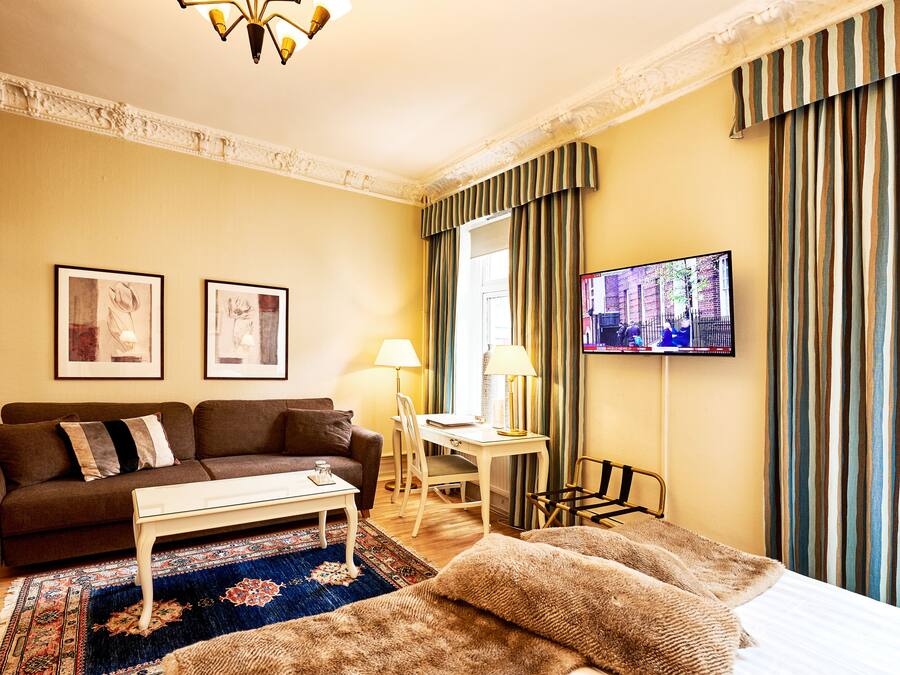 A hotel room with a sofa, a small table, a TV, and a bed with a blanket.