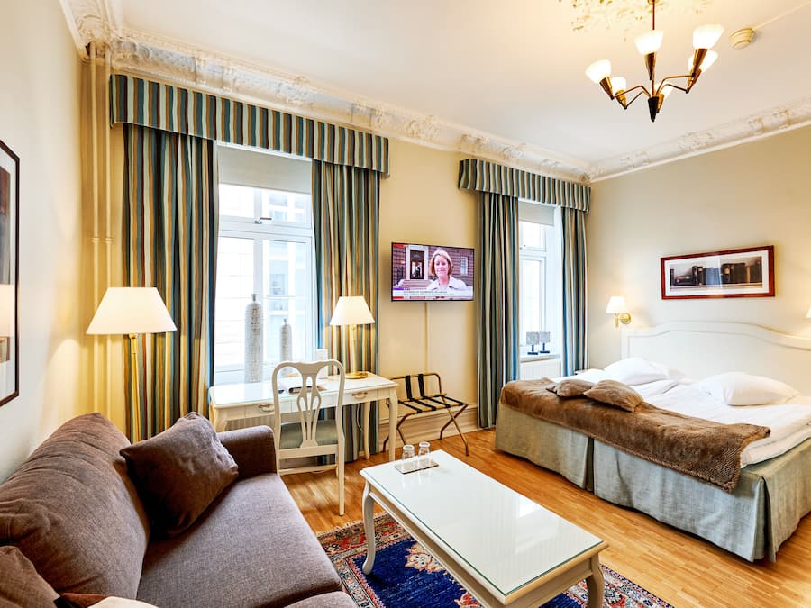 A hotel room with a bed, a sofa, a desk, and a television.