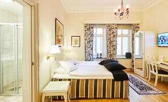 Habitación de hotel con cama, lámparas de noche, escritorio con silla, televisor y ventana con cortinas.