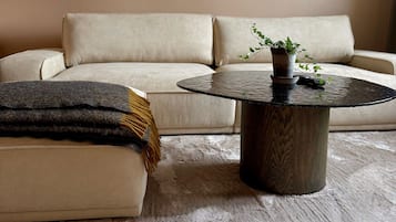 Ett vardagsrum med en beige soffa, ett runt soffbord med en växt och ett inramat konstverk på väggen.