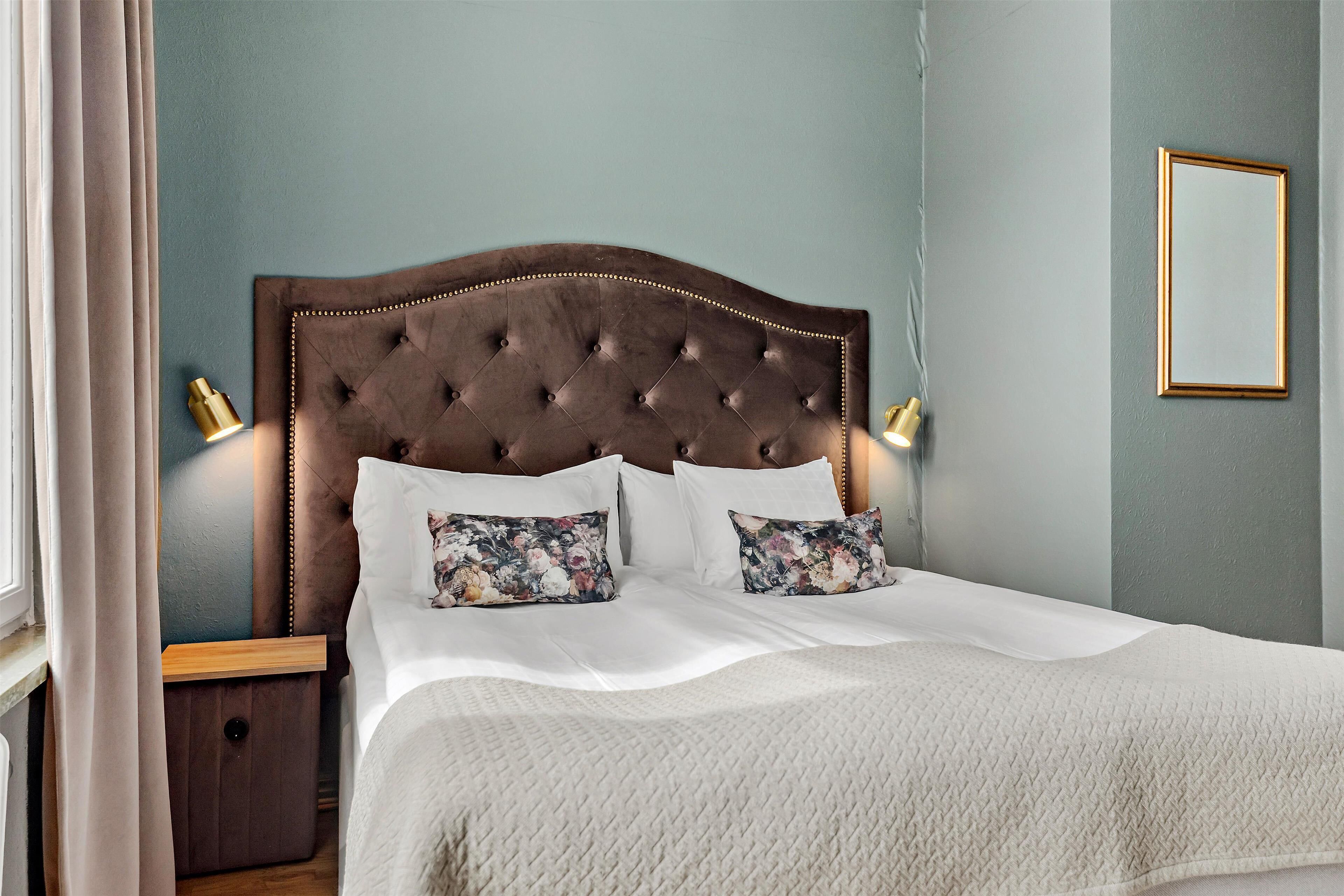 A neatly made bed with a tufted headboard, two bedside lamps, and floral-patterned pillows.
