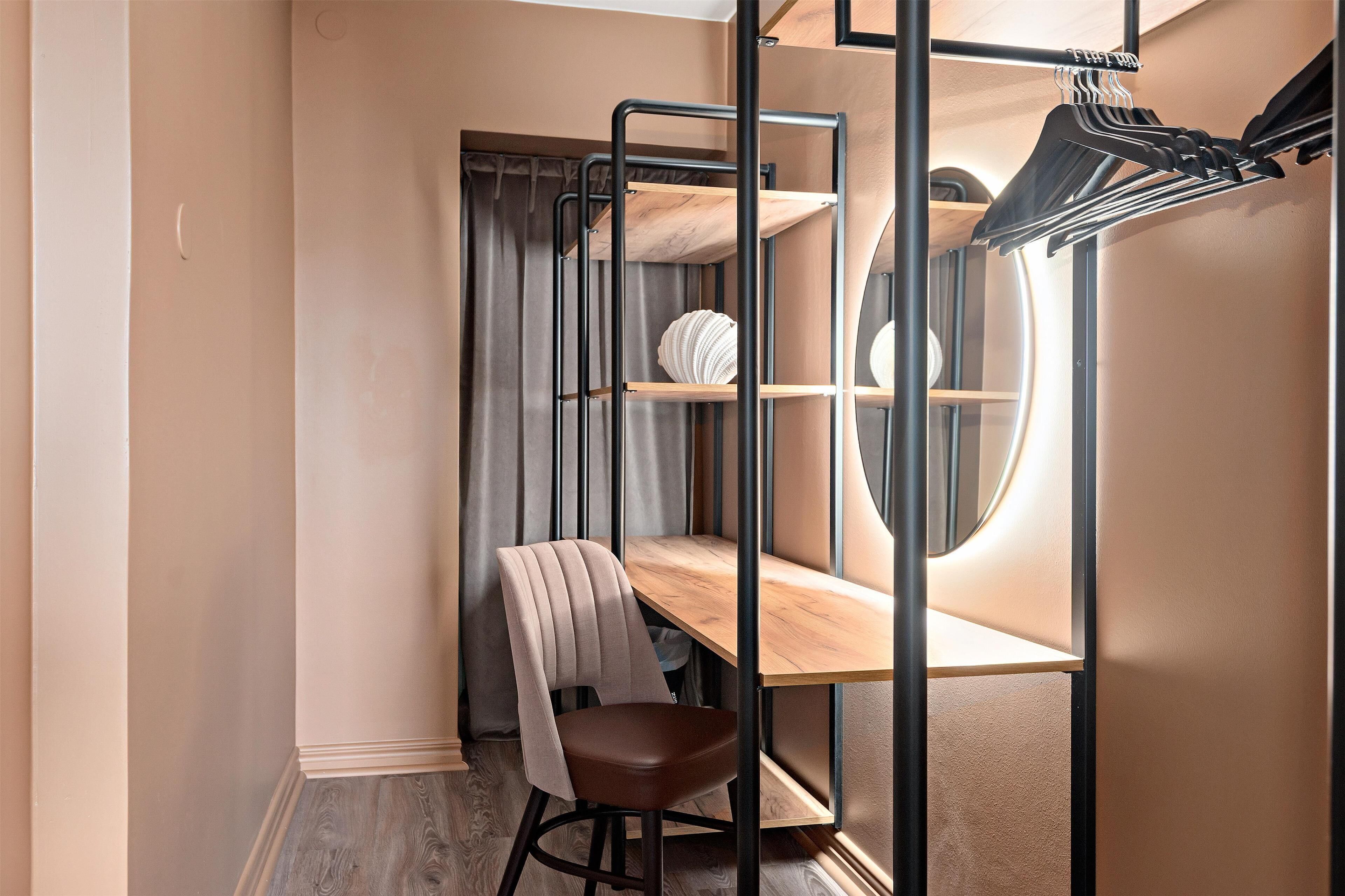 A bunk bed with a wooden desk and chair, a hanging rack, and a window with a circular view.