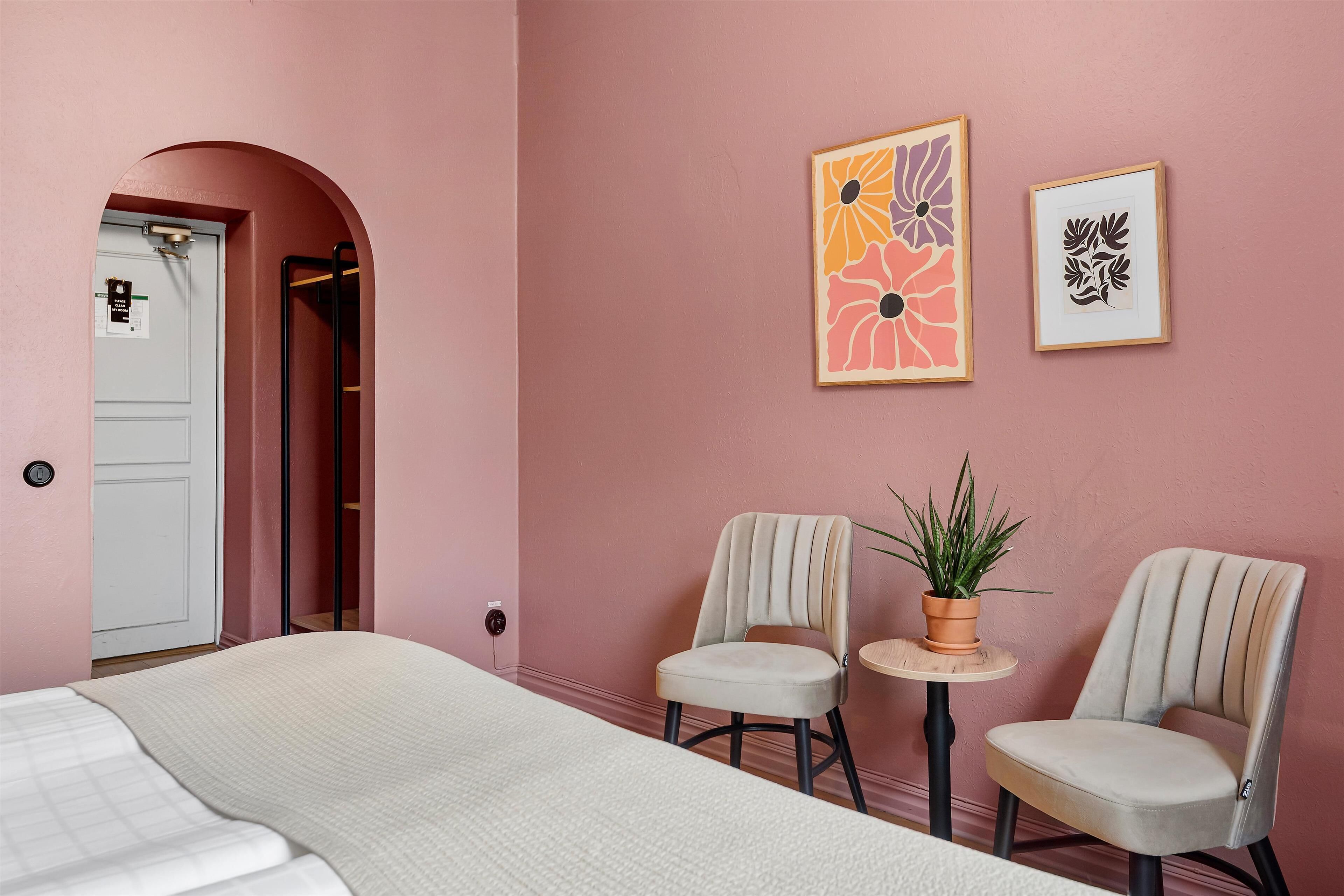 A bedroom with a bed, two chairs, a small table with a plant, and two framed artworks on the wall.