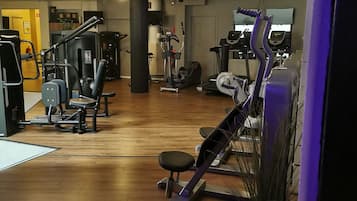 A gym with various exercise equipment, wooden flooring, and a potted plant.