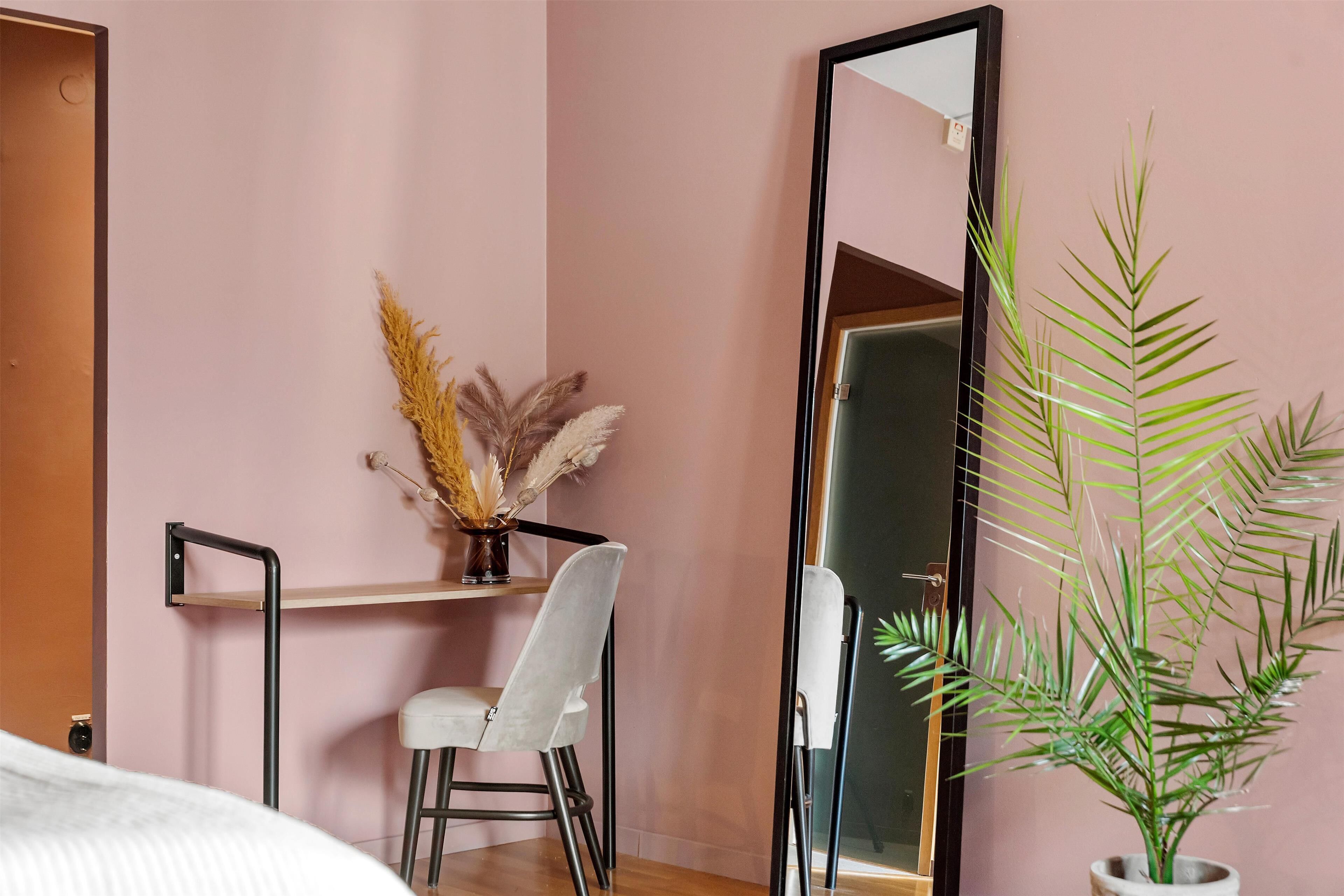 A room with a bed, a desk with a chair, a mirror, and a potted plant.