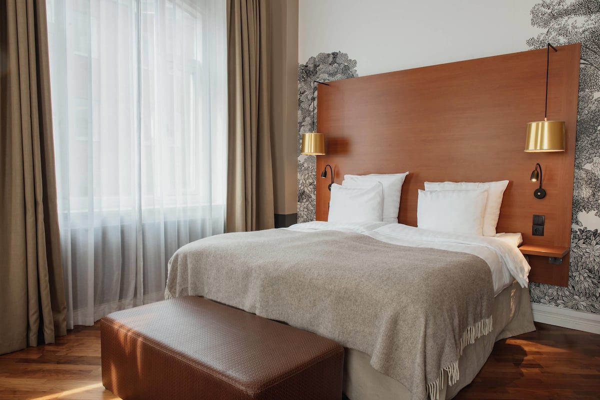 A hotel room with a large bed, a wooden headboard, two wall-mounted lamps, and a bench.