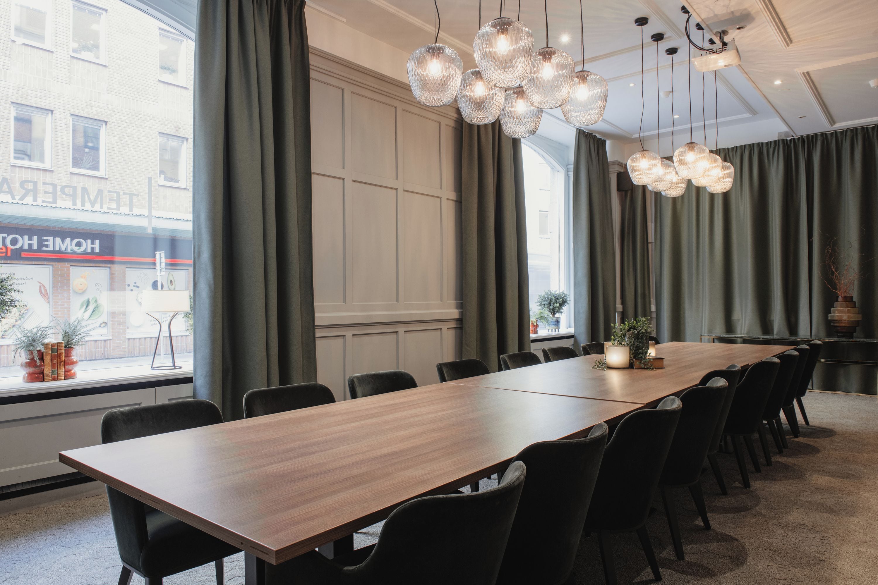 Une salle de conférence avec une longue table en bois, des chaises noires et de grands lustres en cristal suspendus au plafond.