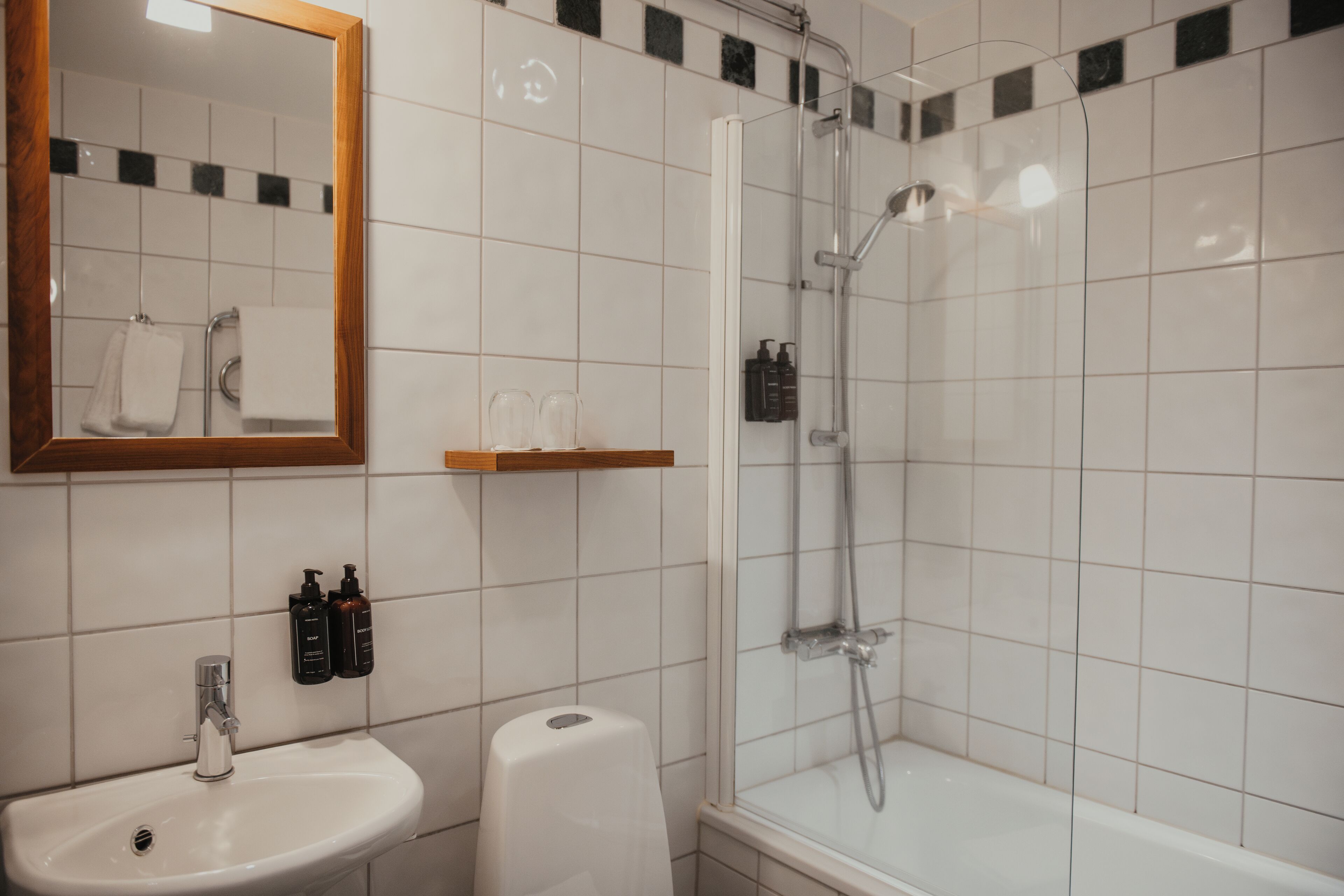 A bathroom with a sink, mirror, shower, and toiletries.