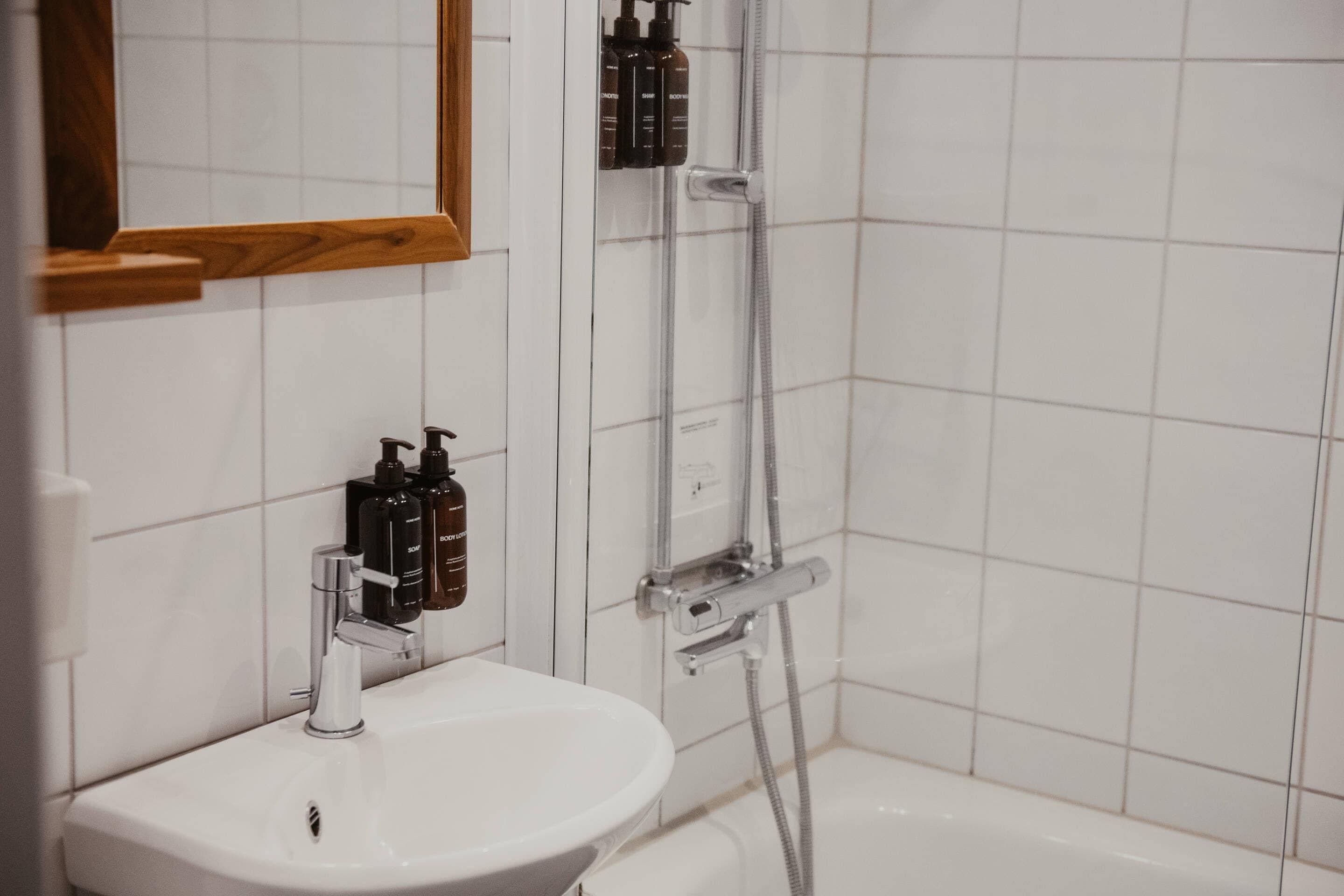 Un baño con lavamanos blanco, un espejo y zona de ducha.