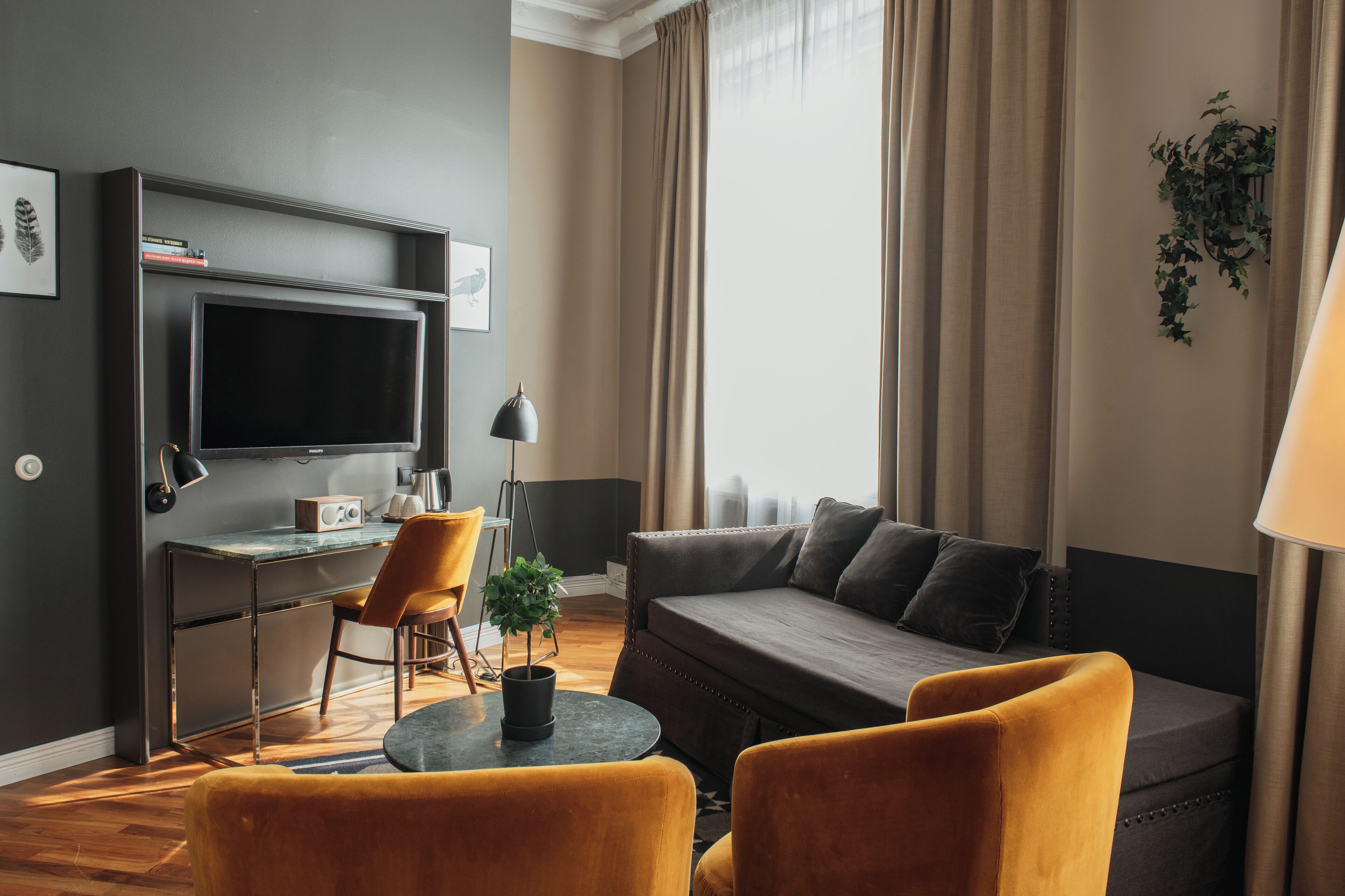 A modern living room with a sofa, two armchairs, a small table, a TV, and a desk with a chair.