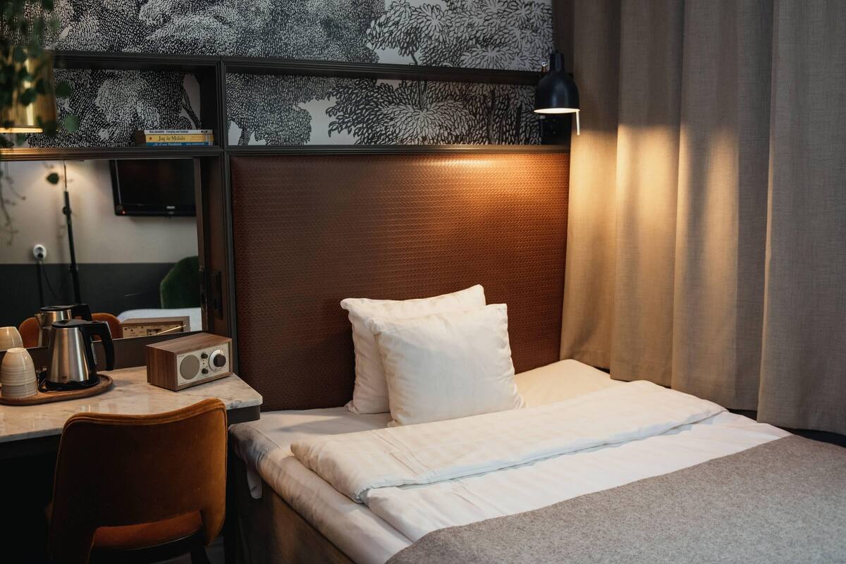 A hotel room with a bed, a desk with a radio, a coffee maker, and a bookshelf.