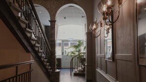 Un pasillo con una escalera, una planta y apliques de pared.