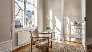 A room with a large window, a chair, a small table with a plant, and a radiator.