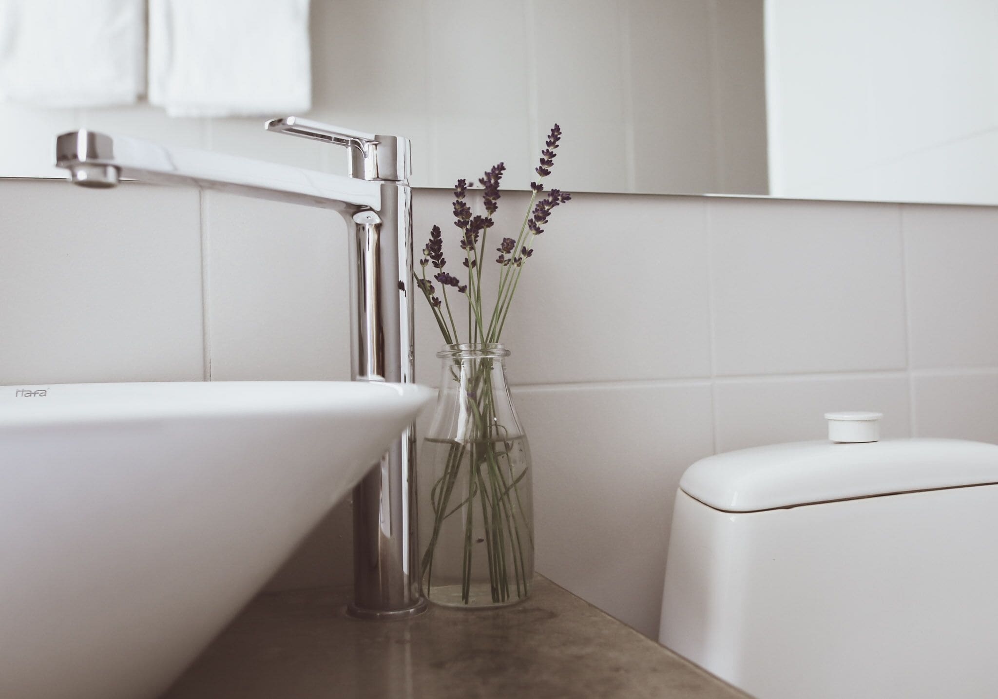 A bathroom with a white sink, a glass vase with lavender flowers, and a toilet.