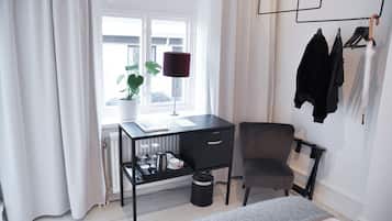 A modern room with a desk, chair, radiator, potted plant, and a coat rack with hangers.