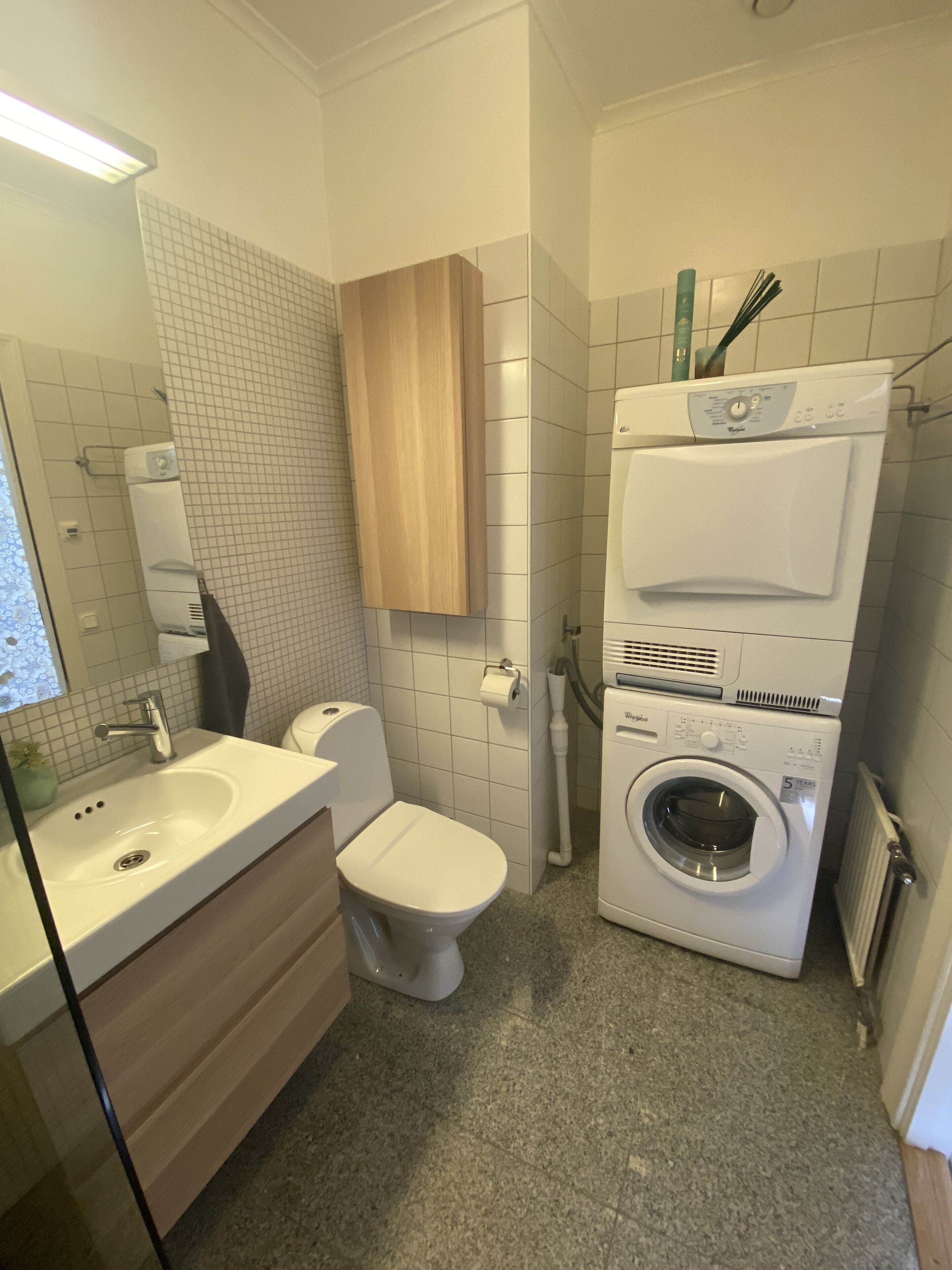 Et lille badeværelse med vask, toilet og stablet vaskemaskine og tørretumbler.