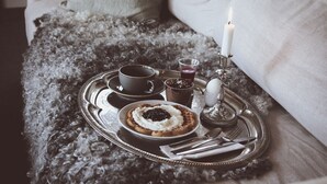 A cozy living room with a grey fluffy rug, a tray with snacks, a candle, and a window with a plant.