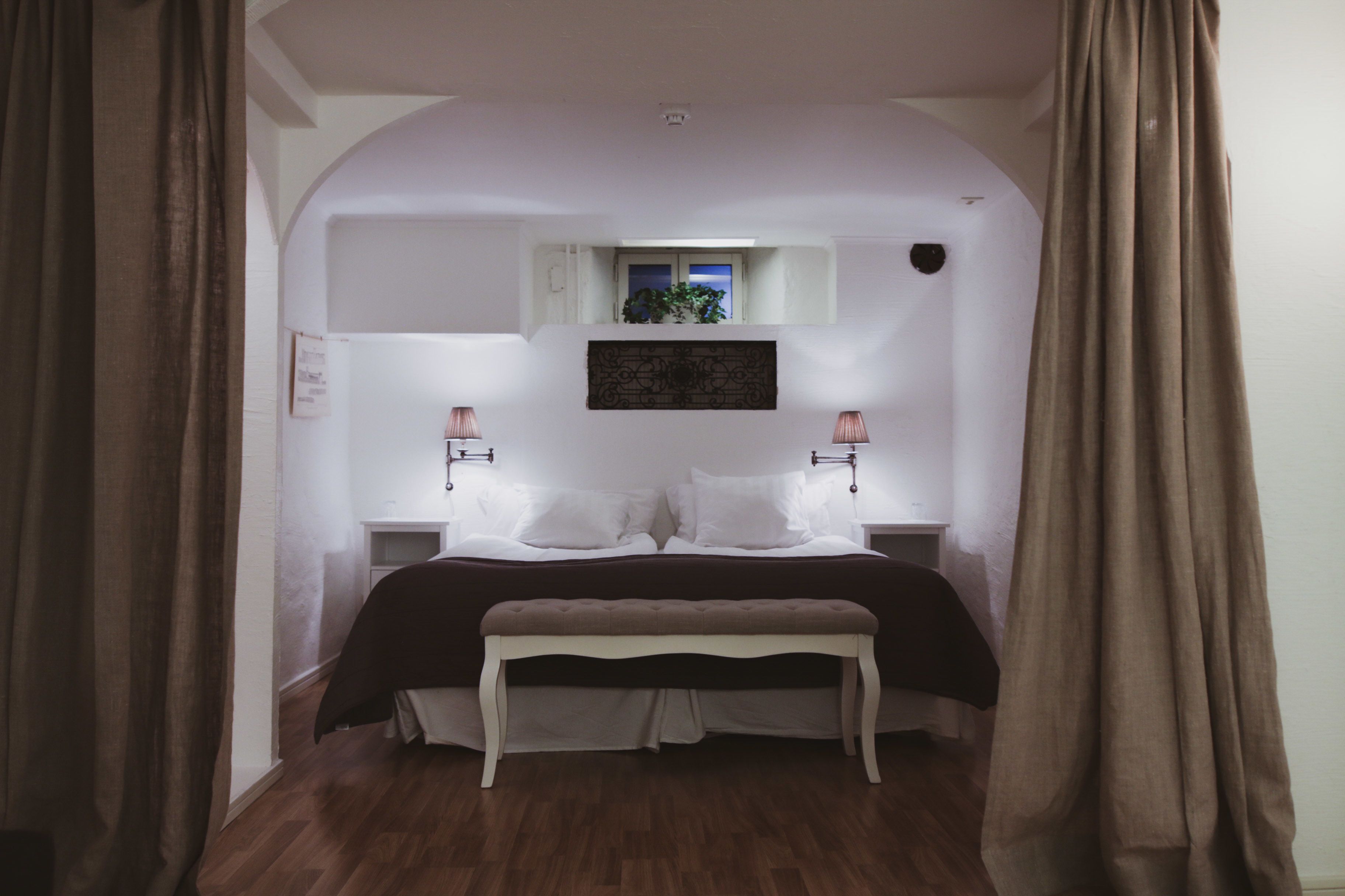 A bedroom with a bed, two bedside tables, a bench, a window with a view, and a wall-mounted artwork.