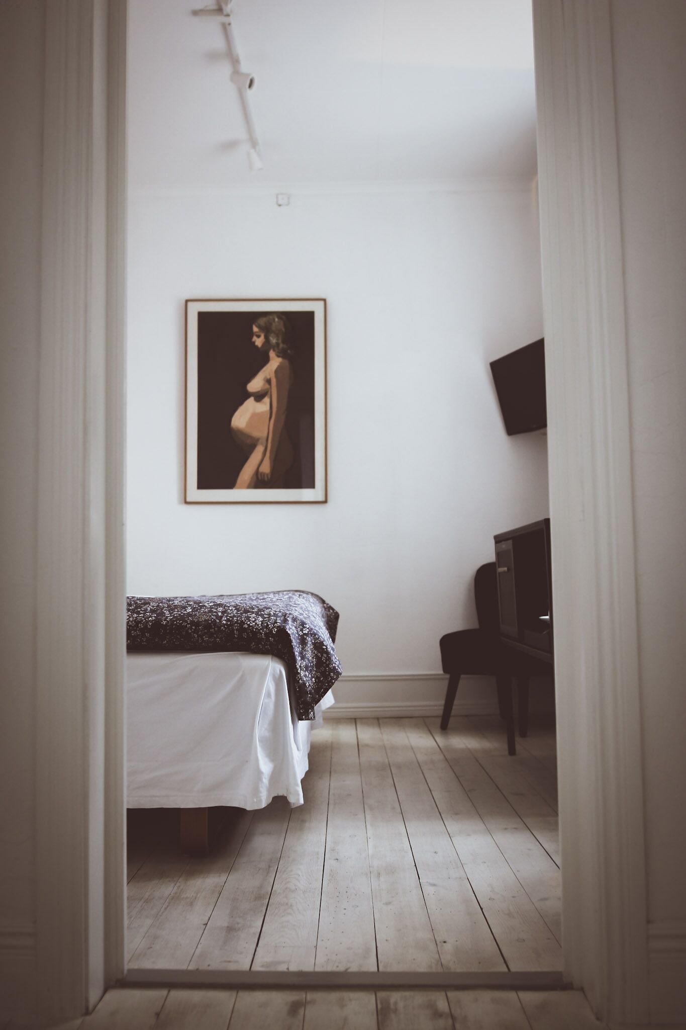 A bedroom with a bed, a framed picture on the wall, a television, and a chair.