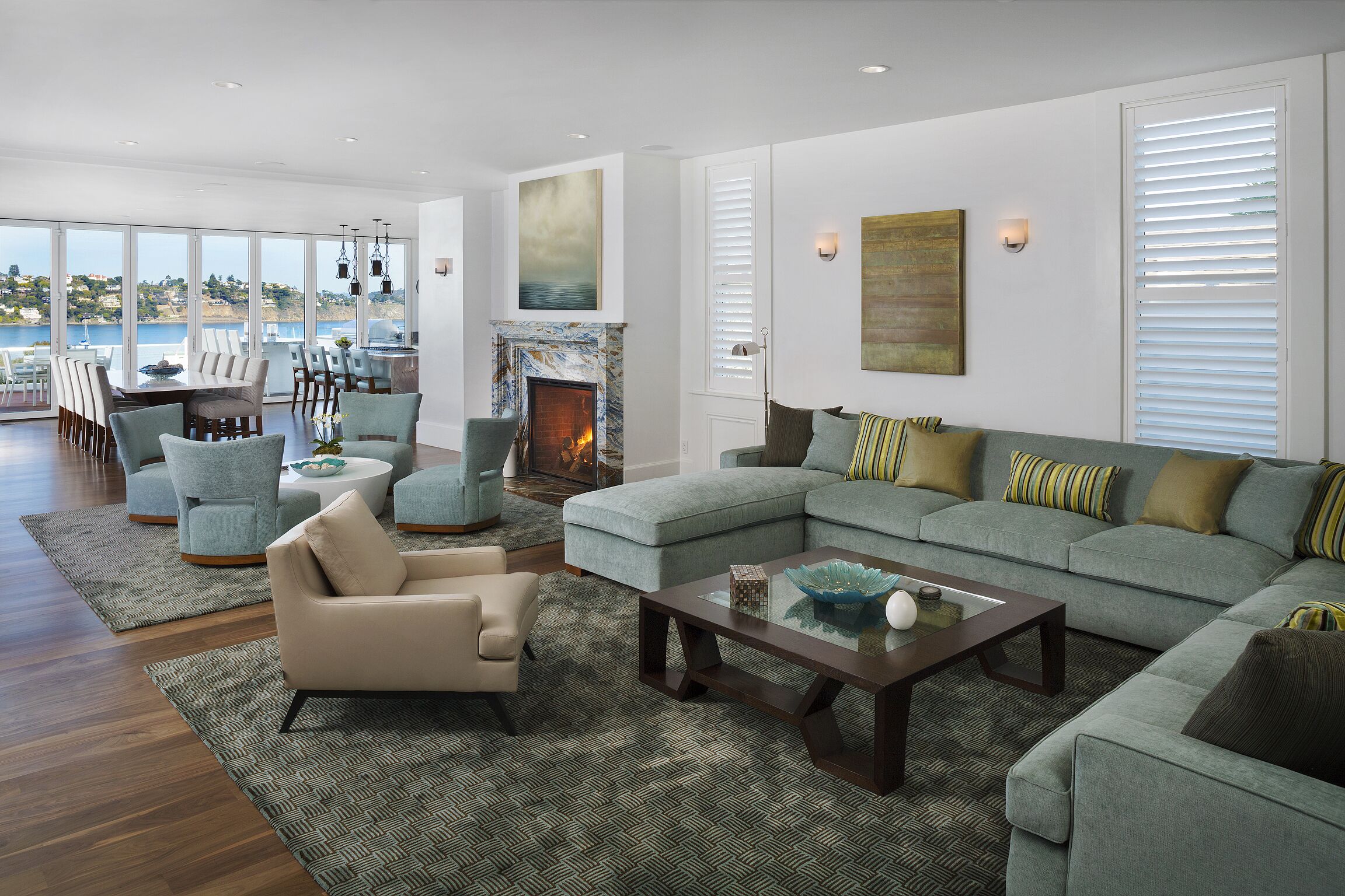 A spacious living room with a large sectional sofa, a fireplace, and a view of the sea.