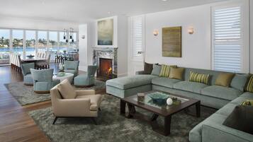 A spacious living room with a large sectional sofa, a fireplace, and a view of the sea.