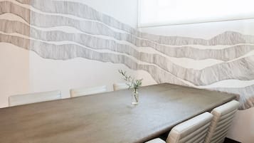 A conference room with a wooden table and beige upholstered chairs. A small vase with a plant is on the table. The wall features a wavy, textured design.