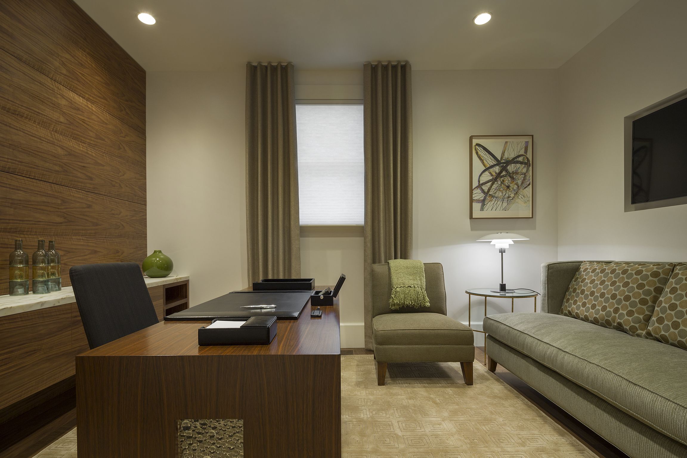 A modern hotel room with a wooden desk, a comfortable sofa, a small side table, and a lamp.