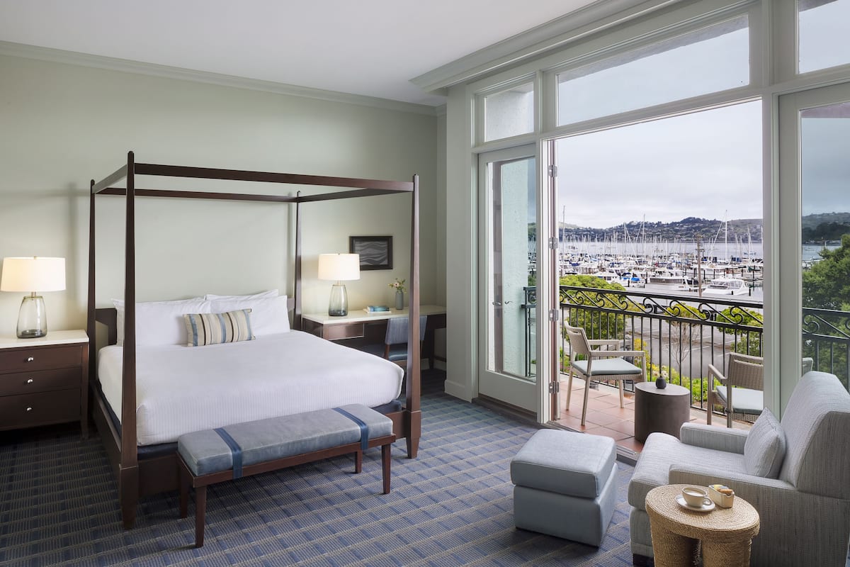 Ein Hotelzimmer mit Himmelbett, einem Balkon mit Blick auf eine Marina sowie einer Sitzecke mit Sofa und Sesseln.