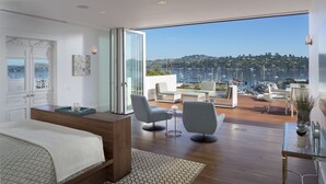 A modern bedroom with a large bed, a desk, and a view of a marina.