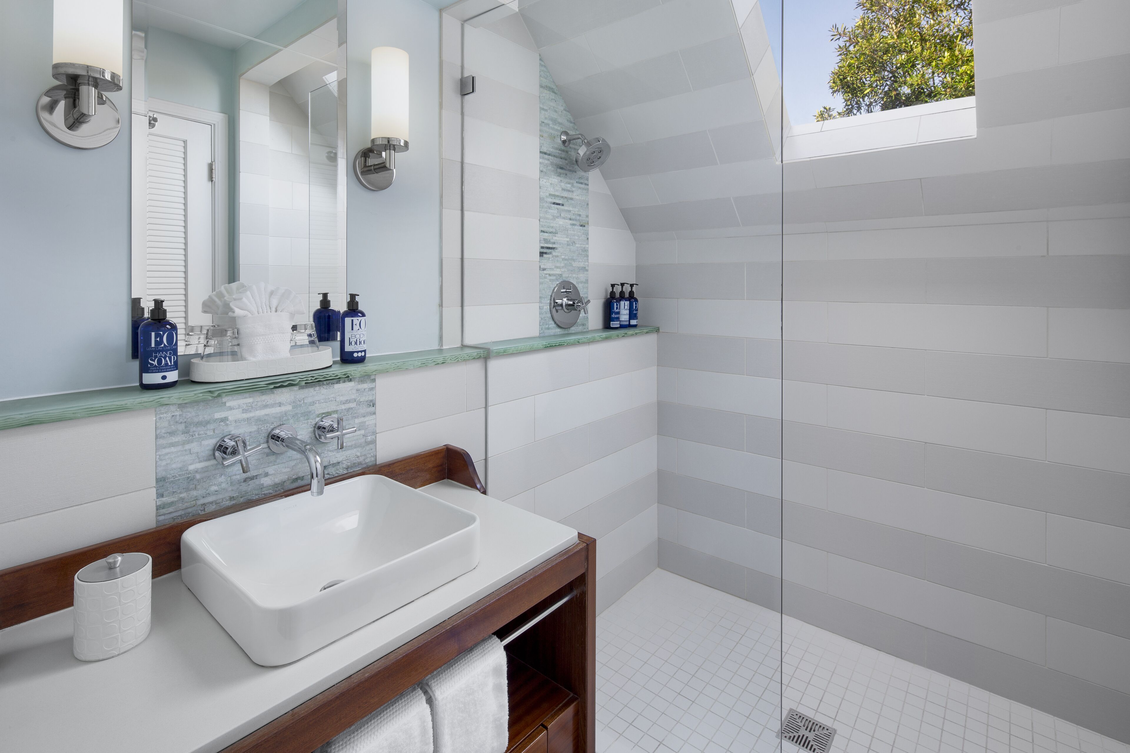 A modern bathroom with a large white sink, a glass shower enclosure, and a skylight.