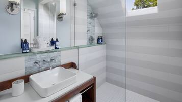A modern bathroom with a large white sink, a glass shower enclosure, and a skylight.