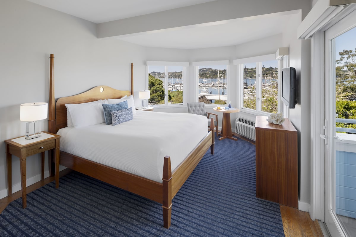 Ein Hotelzimmer mit einem großen Bett, einem Fernseher, einem Schreibtisch und Blick auf den Hafen.