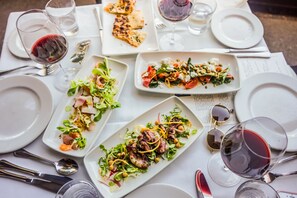 A table set for a meal with various dishes, glasses of red wine, and cutlery. - Casa Madrona Hotel & Spa (Sausalito)