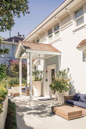 A covered patio area with outdoor furniture, potted plants, and a white building in the background. - Casa Madrona Hotel & Spa (Sausalito)