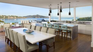 A modern kitchen with a large island, dining area with chairs, and a view of the sea.