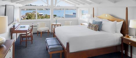 A bedroom with a large bed, a desk, a chair, and a view of the sea.