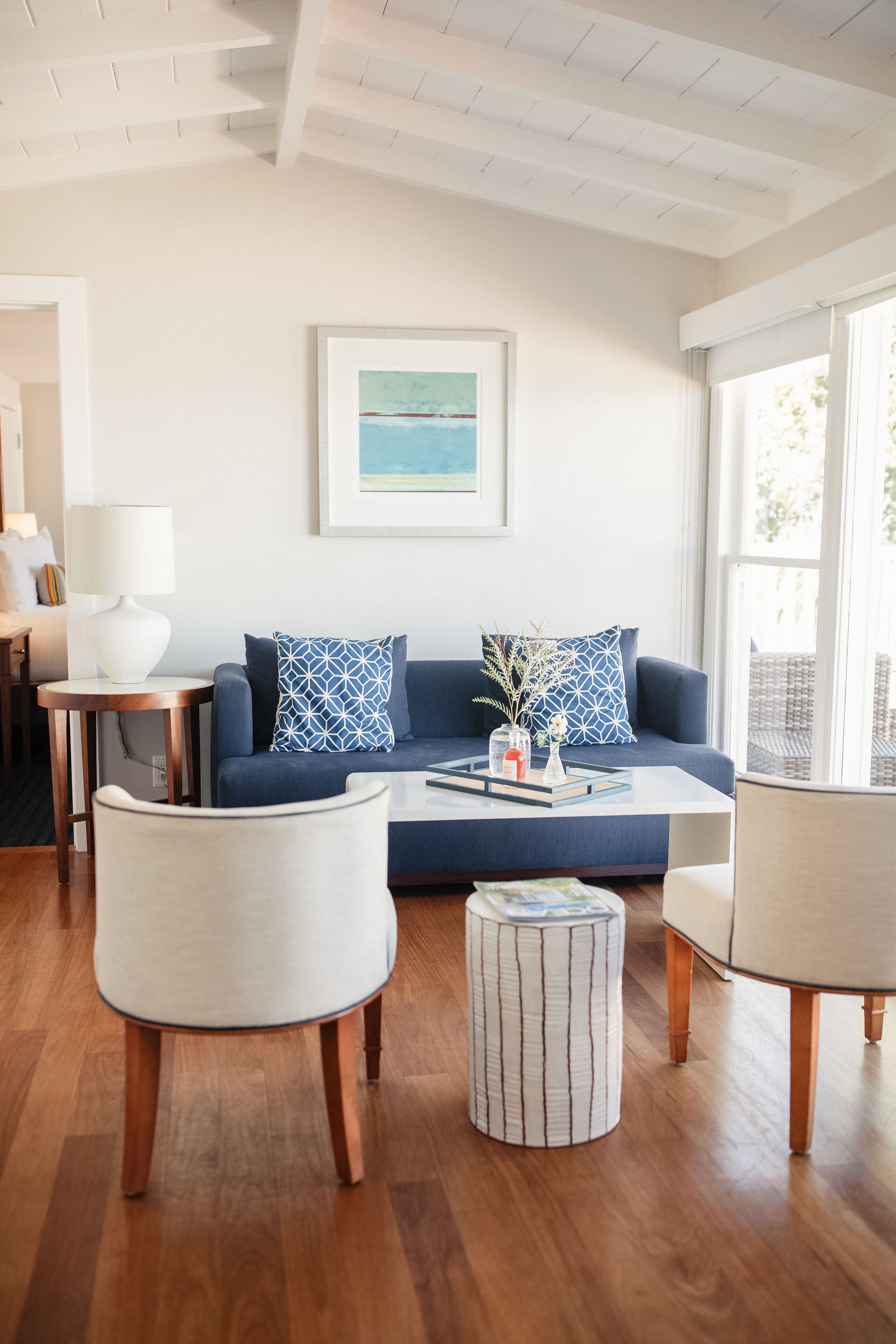 Uma sala de estar moderna com um sofá azul, poltronas brancas, uma mesa de centro e um quadro na parede.