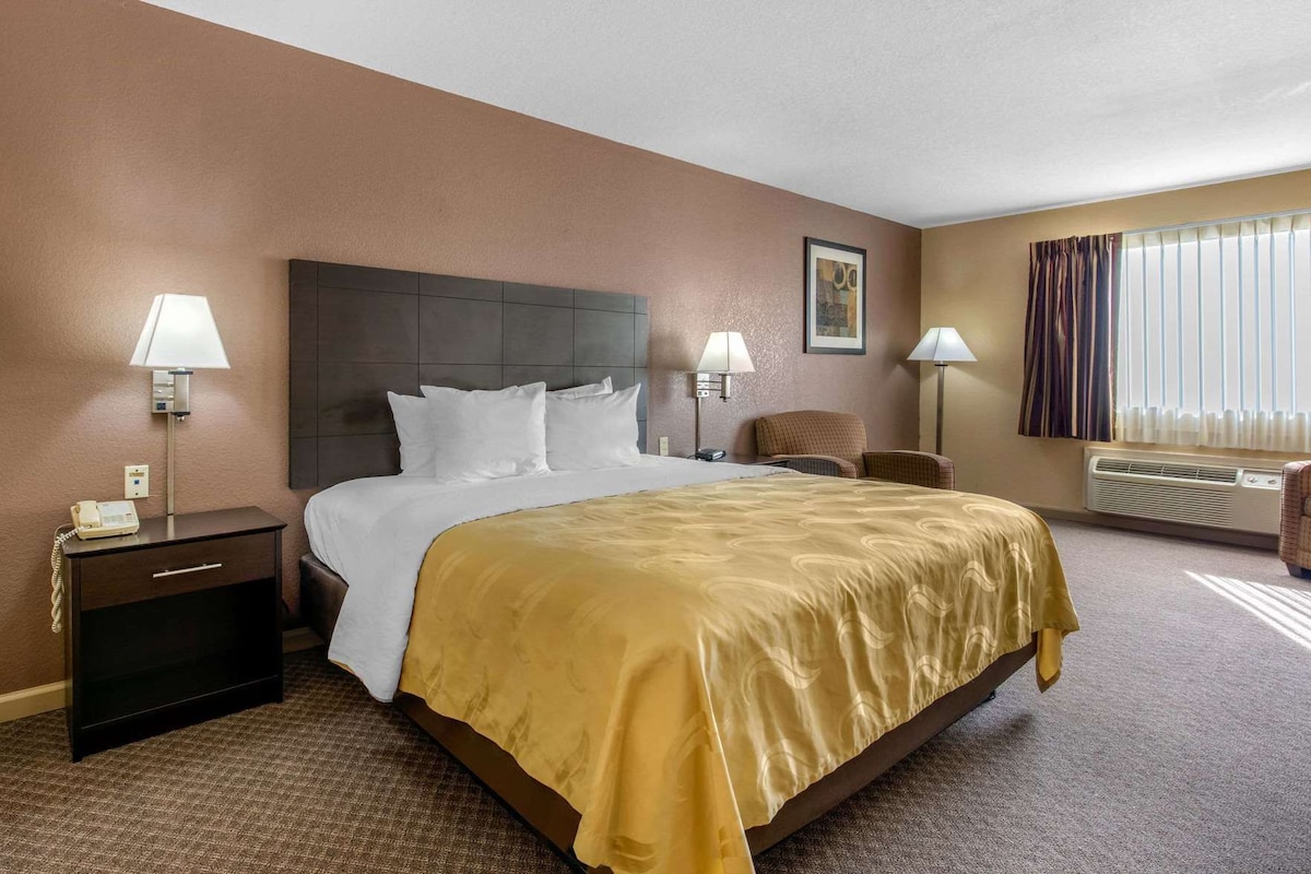 A hotel room with a bed, bedside tables, lamps, a chair, and a window with curtains.