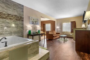 A modern hotel room with a large bathtub, a sofa, a small table, and a TV.