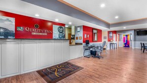 A hotel reception area with a red wall, a reception desk, and a seating area with chairs. - Quality Inn West Memphis I-40 (West Memphis)