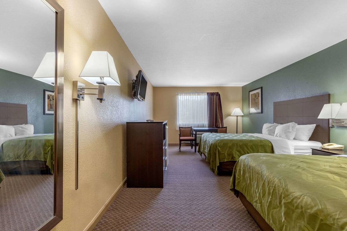 Een hotelkamer met twee bedden, een bureau, een stoel, een televisie en een minibar.