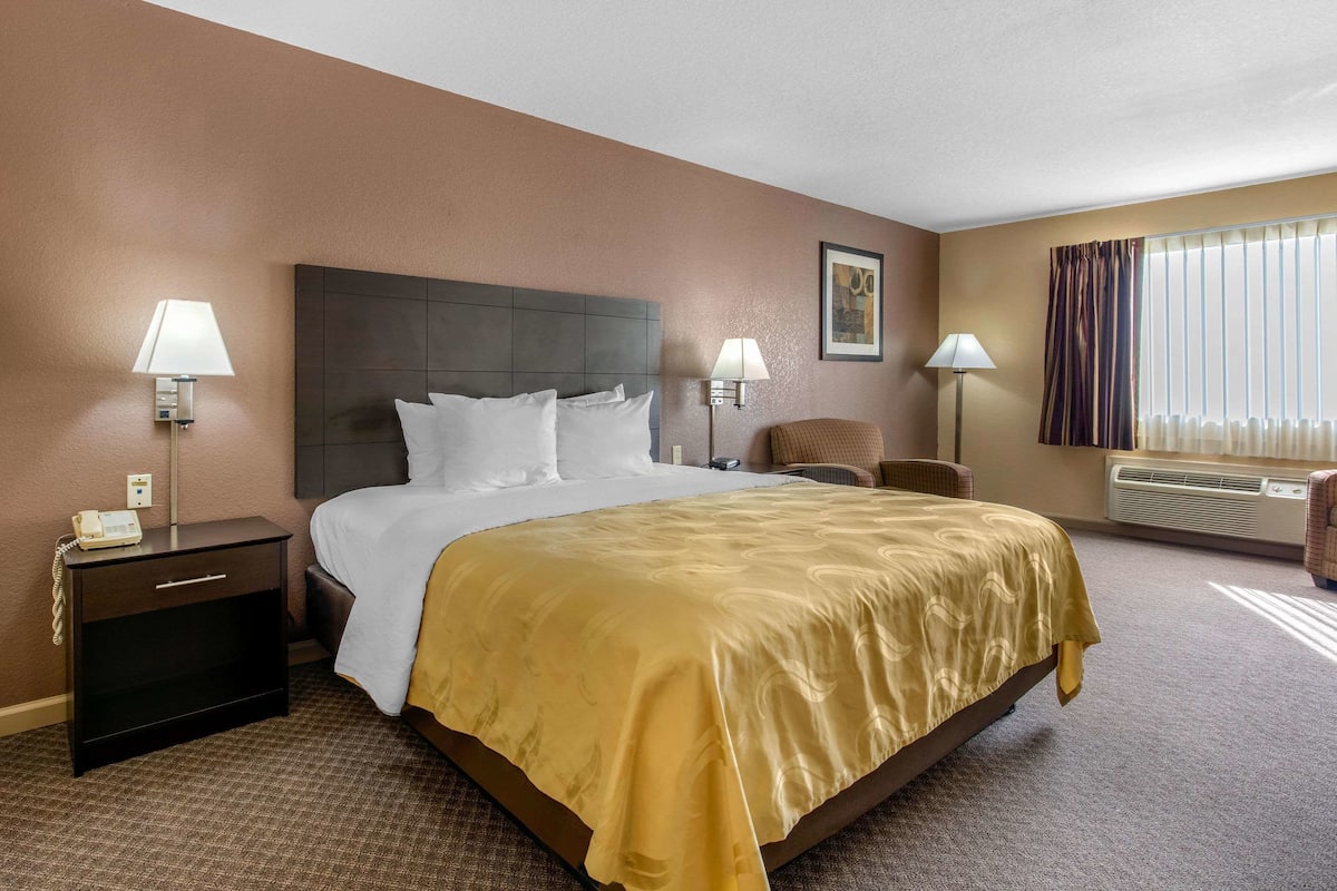 Habitación de hotel con una cama grande, dos mesitas de noche con lámparas, una silla, un escritorio y una ventana con cortinas.