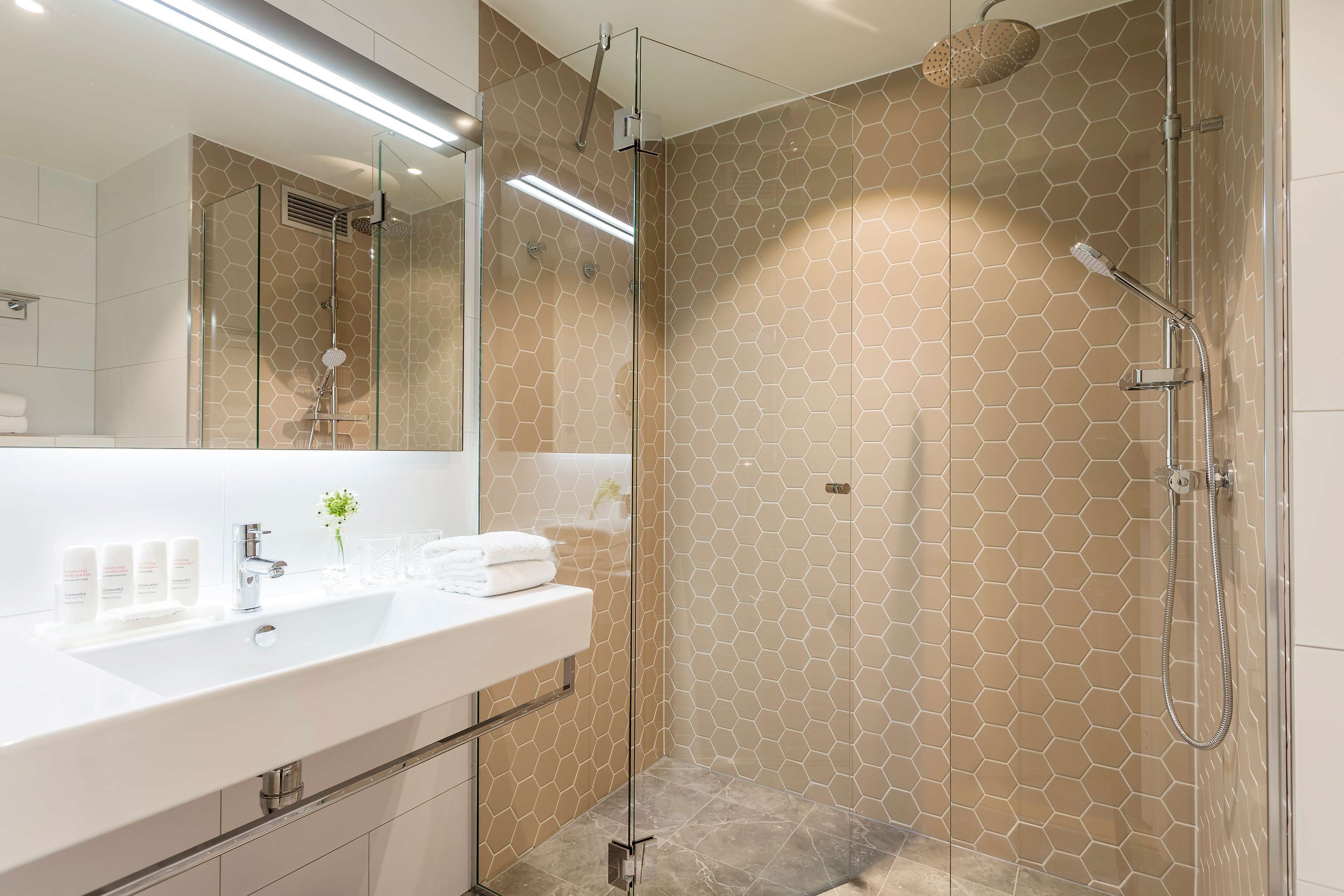 Un bany modern amb dutxa de vidre, un lavabo blanc i un mirall.